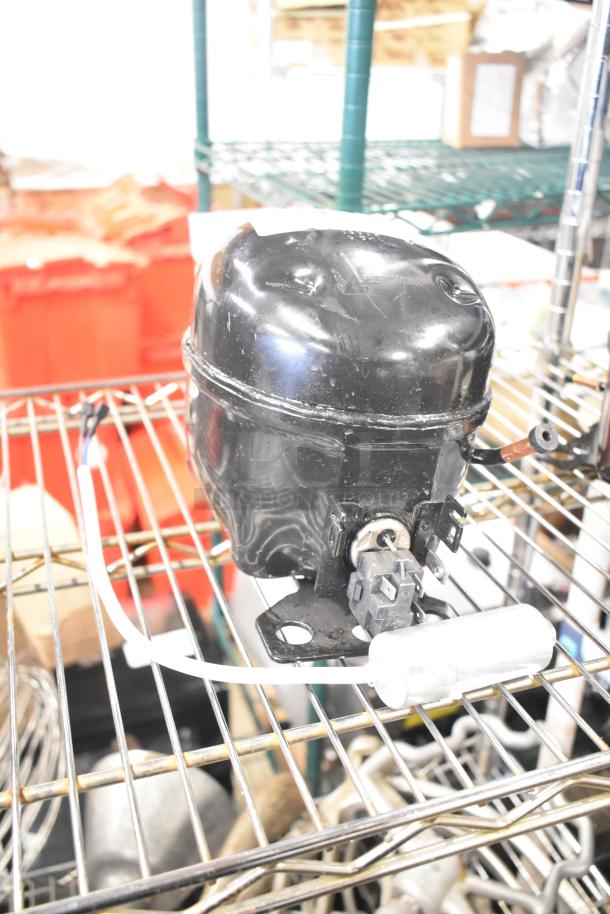 Cubigel NUT70NR Compressor, black, for 115-127 volts, 1 phase, gently used condition, on metal shelf.