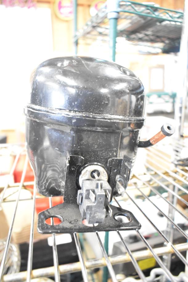 Cubigel NUT70NR Compressor in black, 115-127V, 1 phase, shown on a metal shelf, in good condition.