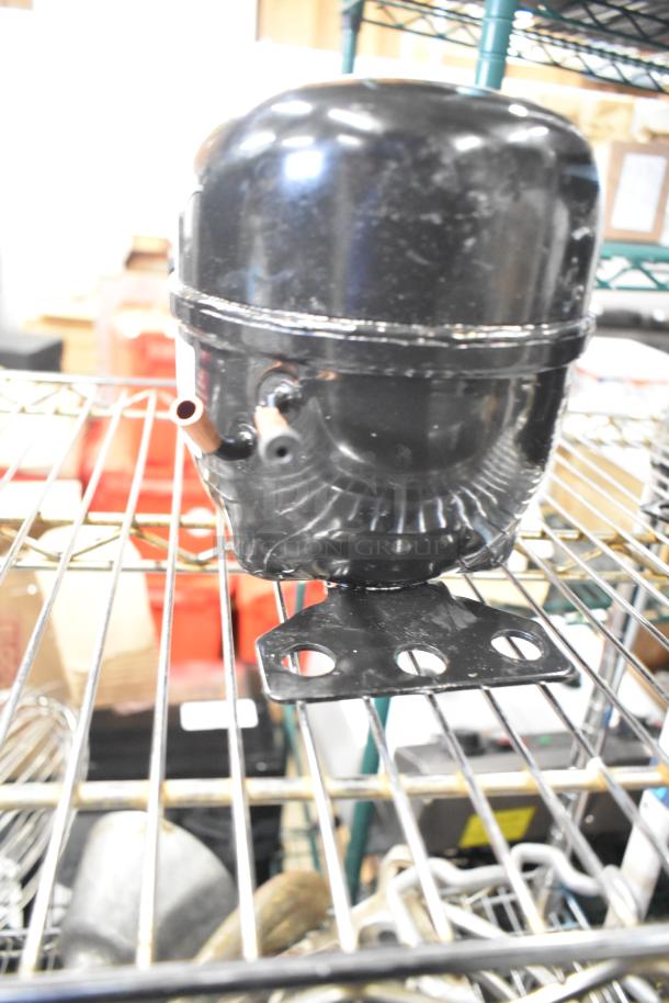 Cubigel NUT70NR compressor, black, 115-127 volts, 1 phase, appears in good condition on a metal shelf.