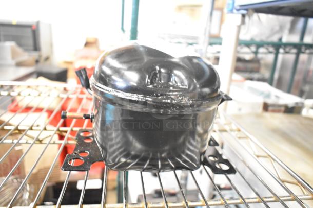 LG TS24LACG Compressor, 115 Volts, 1 Phase, black, used, on metal rack in a storage area.