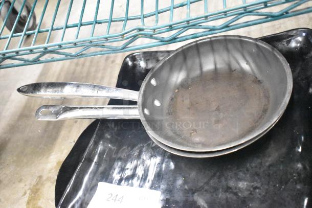 Two stacked skillets with stainless steel handles, showing signs of use. Auction label reads "244 QTY."