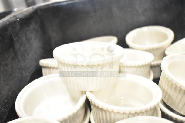 White ceramic ramekins stack inside a black poly bus bin. Ramekins feature a ribbed design, in good condition.