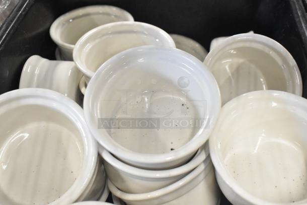Collection of white ceramic ramekins in good condition, stacked in black poly bus bins. Suitable for kitchen use.