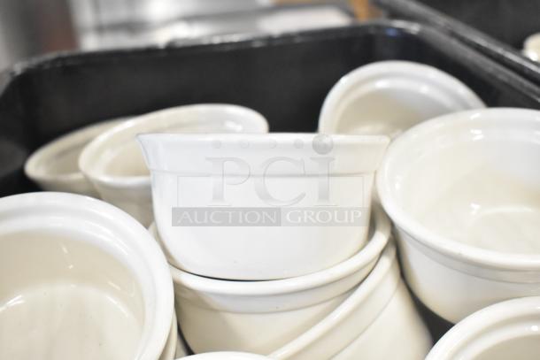 White ceramic ramekins in a bus bin, part of a tiered lot auction. Ramekins appear in good condition.