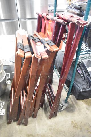 Five wooden serving tray stands with dark finish, in used condition. Straps visible for secure folding.