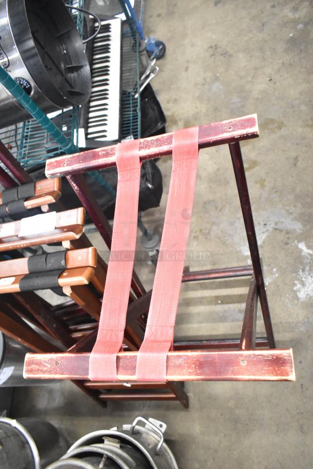 Five wooden serving tray stands with red fabric straps, showing wear and prominent wood grain. Ideal for catering use.