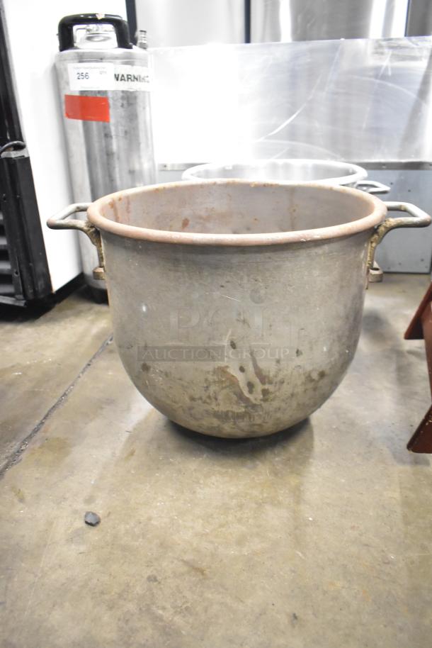 Large metal mixing bowl with handles, showing signs of wear and patina, indicative of high durability and use.
