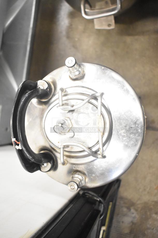 Stainless steel ball lock keg with black handle, visible lid latches, and labeled “IN” and “OUT” ports, in used condition.