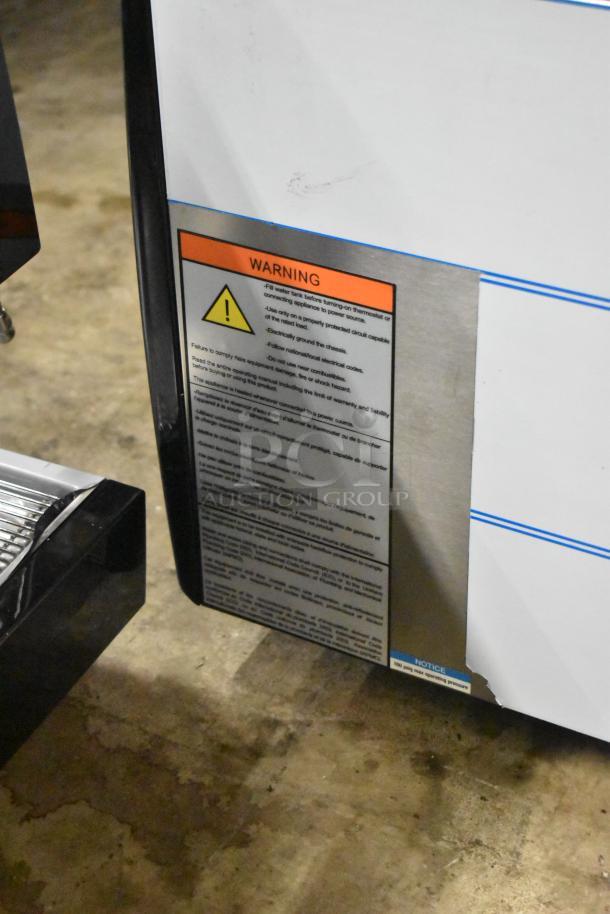 BRAND NEW Gaggia MGV293NPU Vetro Black 3 Group Espresso Machine, 220/230V, scratch and dent condition, warning label visible.