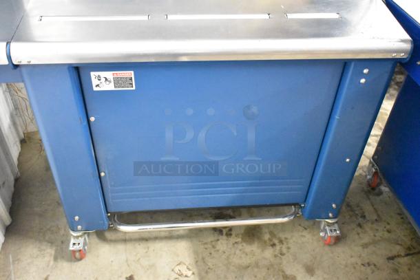 Polychem PC1000 automatic strapping machine, blue, on casters, stainless steel top, 115V, 1 phase, warning label visible.