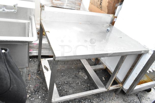 Stainless steel commercial table with backsplash. Shows signs of wear. Ideal for kitchen or industrial use.