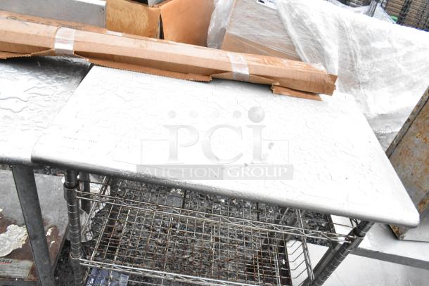Commercial table with three wire under shelves on casters, metal surface, sturdy construction, some signs of wear.