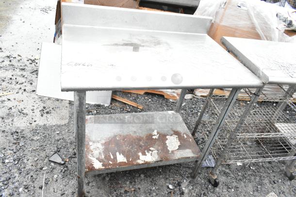 Commercial table with under shelf and backsplash, shows wear and rust on lower shelf. Sturdy metal frame, suitable for heavy-duty use.