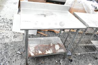 Commercial table with under shelf and backsplash, shows wear and rust on lower shelf. Sturdy metal frame, suitable for heavy-duty use.