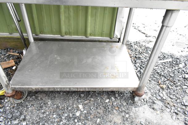 2-tier stainless steel cart on commercial casters, showing signs of wear. Ideal for industrial use.