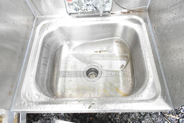 Commercial single bay stainless steel wall mount sink with faucet, handles, and side splash guards, in used condition.