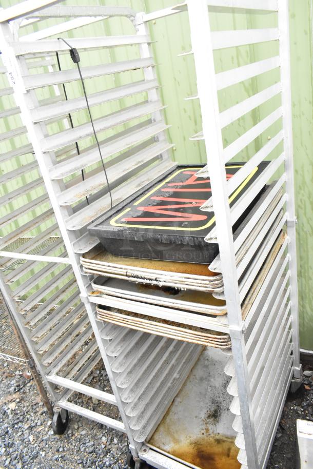 Commercial pan transport rack with contents, including baking pans, on sturdy casters. Shows wear from use.