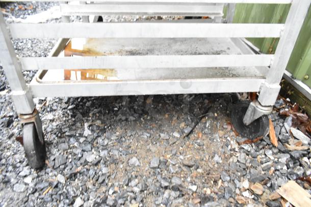 Commercial pan transport rack with casters, holding several baking pans. Visible wear on the frame and casters.