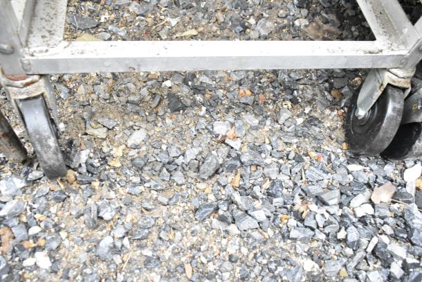 Commercial pan transport rack with sturdy metal frame and heavy-duty casters on gravel surface.