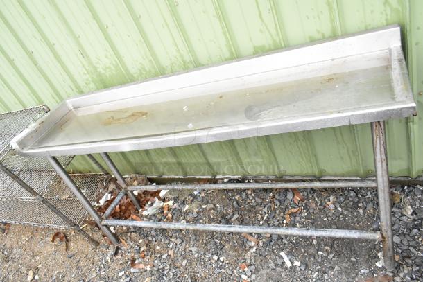 Industrial metal table with a raised lip, showing signs of rust and discoloration, against a green metal wall.