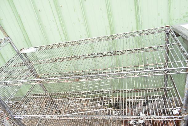 Chrome finish 3-tier wire shelving unit, slightly rusted, outdoor setting. BUYER MUST DISMANTLE. Consider freight charges.