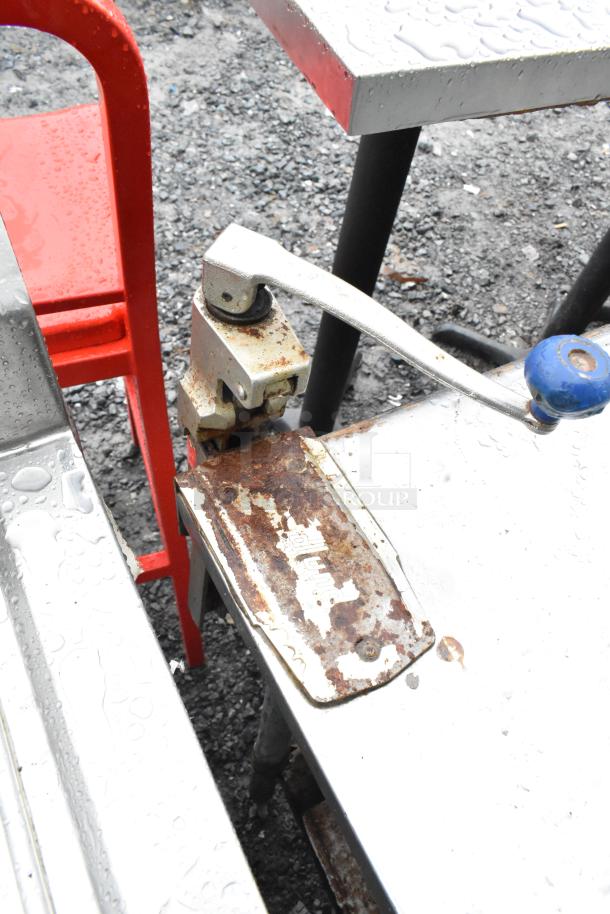 Commercial table with mounted can opener; visible rust and wear on metal surface; includes an under shelf.
