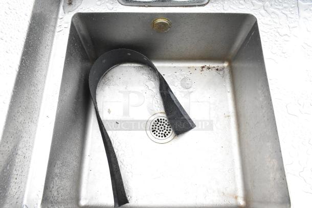 Stainless steel sink basin of a commercial soda station with water dispenser, showing signs of wear.