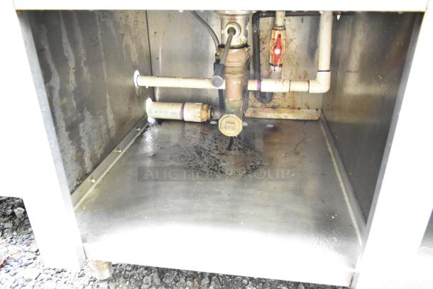 Commercial soda station underside view showing plumbing components, including pipes and valves. Visible wear and staining.