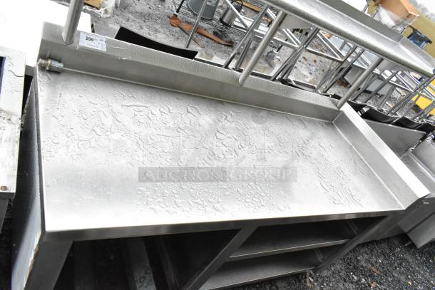 Commercial stainless steel table with over shelf and under shelves; sturdy, slightly wet surface, ideal for kitchen use.