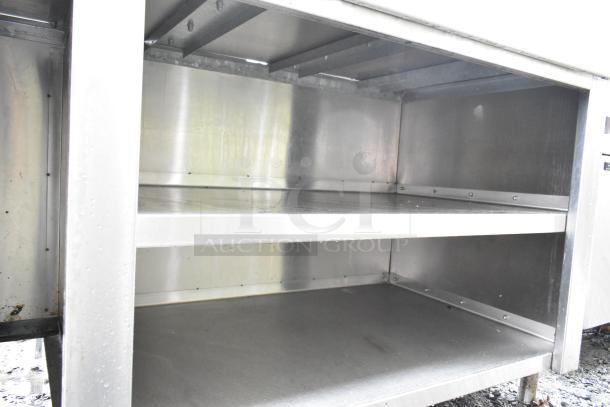 Stainless steel commercial table with over shelf and under shelves, sturdy construction, suitable for kitchen use.