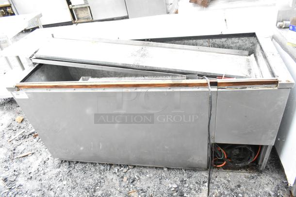 Commercial refrigeration unit with open top, metal exterior, visible wear, power cable, and exposed cooling coils.