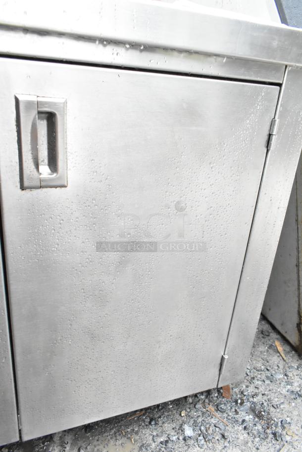 Commercial stainless steel table with bay, over shelf, hinged doors, and undershelf. Used condition with visible wear.