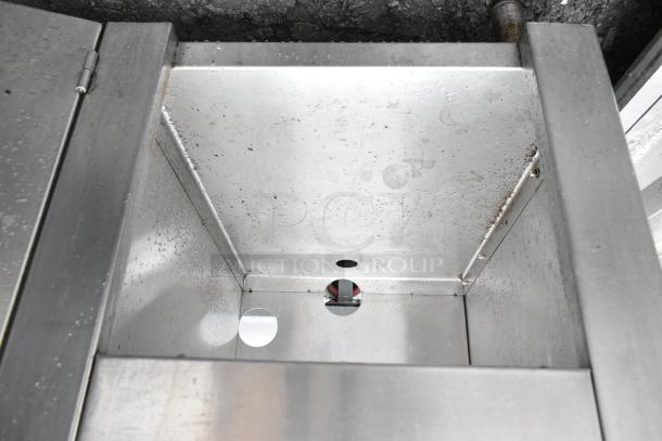 Commercial stainless steel table with bay, overhead shelf, doors, and undershelf. Visible wear and surface markings.