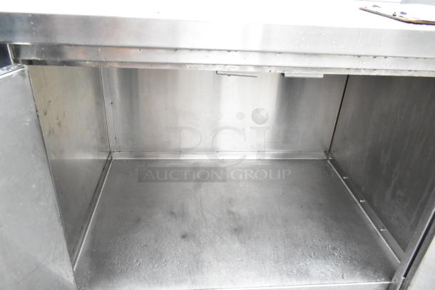 Commercial stainless steel table with bay, overhead shelf, doors, and undershelf. Good condition, suitable for kitchen use.