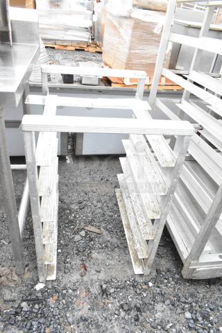 Commercial pan rack with multiple shelves, aluminum construction, outdoor setting, shows signs of wear and use.