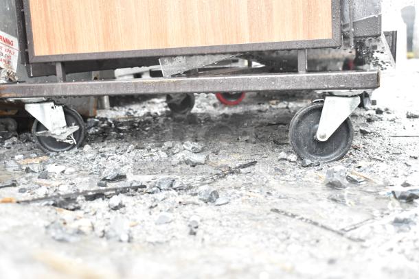 Merchandising rack on casters, wood panel detail, metal frame, used condition, features durable wheels for mobility.