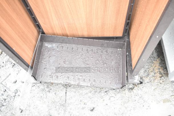 Merchandising rack on casters, featuring a wooden panel design and metal base. Displays slight wear with visible water droplets.
