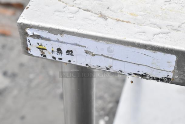 Commercial table with metal under shelf, showing corner detail with wear and remnants of a partially removed label.