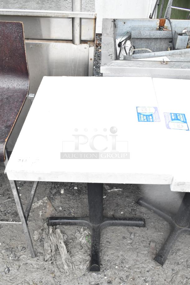 Dining table with white top on black metal base, auction includes five tables. Slight wear visible, suitable for commercial use.