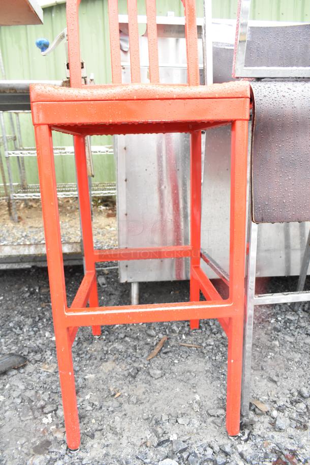 Red metal bar height chair with a sleek design, showing minor weather exposure, ideal for outdoor or industrial settings.