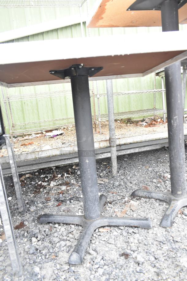 Dining height table with a sturdy black metal base, showing signs of outdoor wear. Ideal for cafes or casual dining areas.