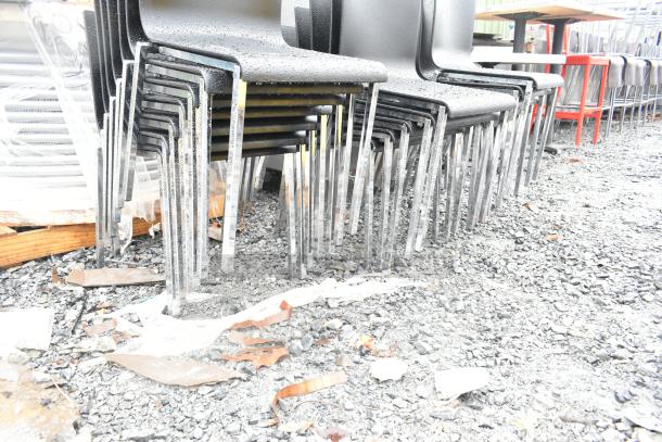 20 dining-height chairs with black seats and chrome finish frames, stacked outdoors. Light wear is visible.