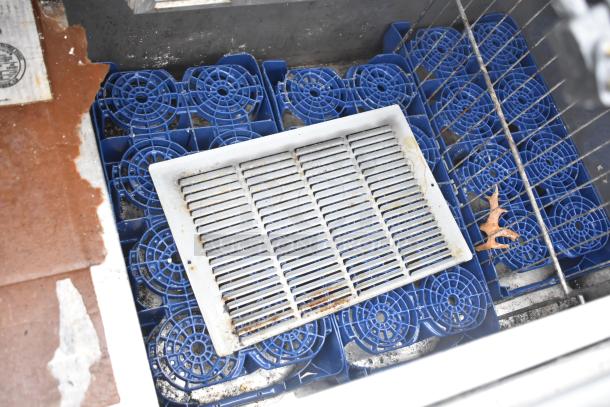 Interior view of Perlick 7260E-SIL-UL cooler showing blue bottle holders and a white drainage grate. Evidence of use visible.