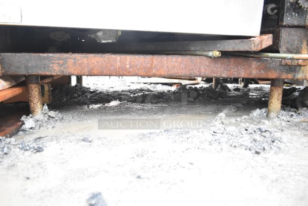 Commercial floor braising pan, visible rust on support legs, outdoor setting, possibly needs maintenance.