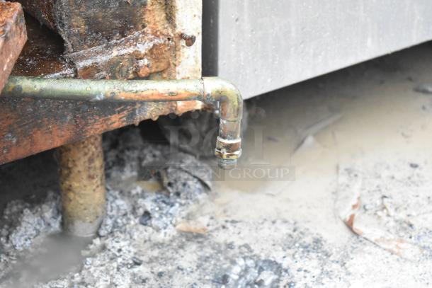 Rusty pipe and base of a commercial floor-style braising pan, showing corrosion and wear.