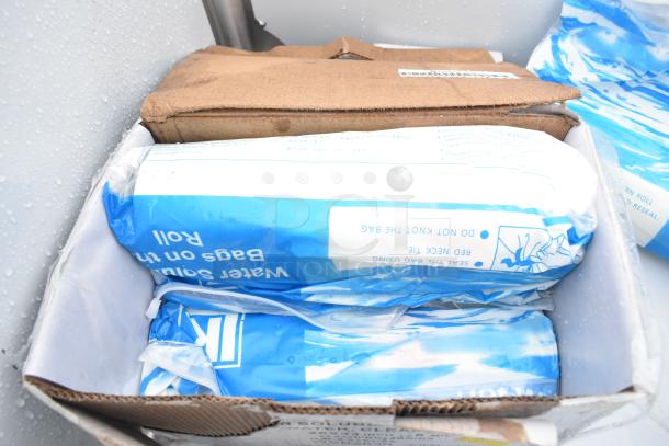 Box containing blue and white packaged water soluble bags, partially opened. Background shows part of a metal item.