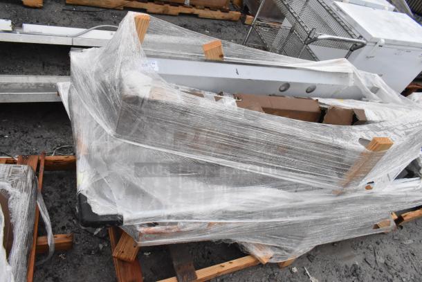 Brand new scratch and dent items wrapped in plastic, including a sink and pot rack. Items secured on wood pallets.