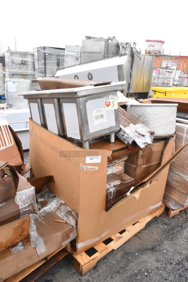 Cardboard box containing 15 brand new scratch and dent items including a metal sink and grease trap on a pallet, labelled with inventory tags.