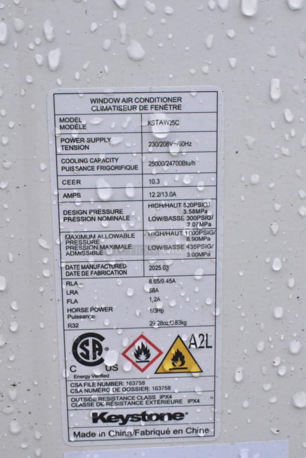 Keystone KSTAW25C window AC label showing 25000/24700 BTU, 208/230V, 1 phase. Manufactured 2025. Energy and safety symbols visible.