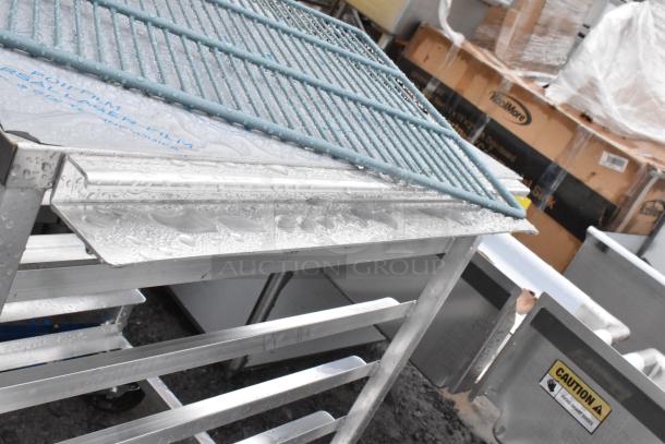 Commercial pan transport rack with metal shelves, shown on weather-resistant commercial casters. Used condition, wet surface visible.